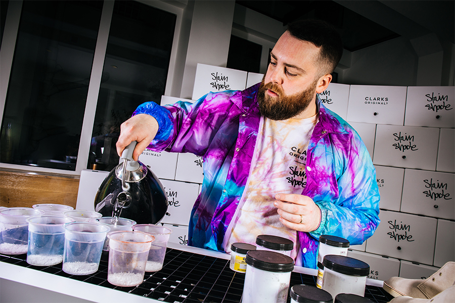 Tie dye artist Stain Shade holding a kettle and using hot water to mix dye, creating bespoke fashion items for Clarks Originals